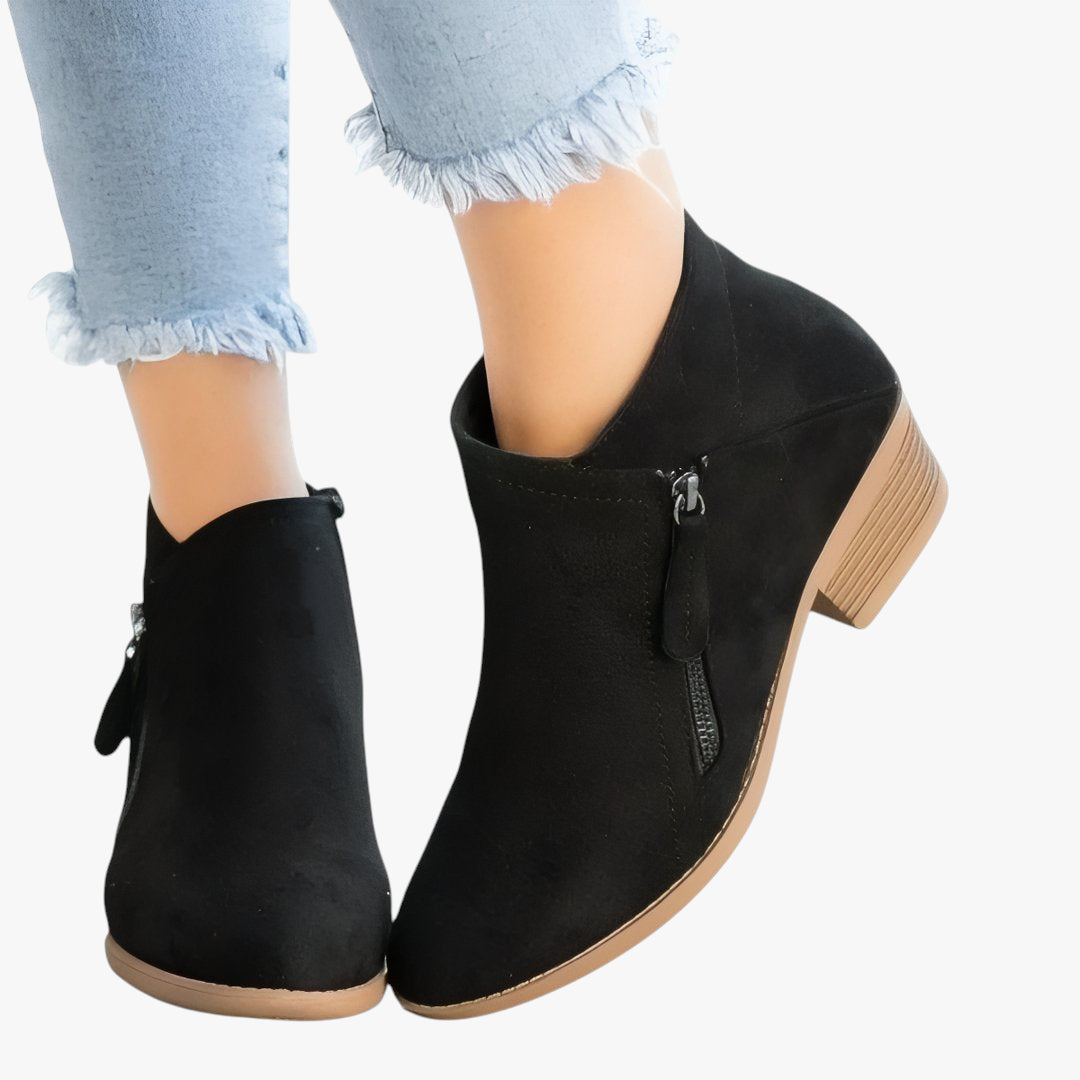 Black ankle boots worn with light blue jeans on a white background