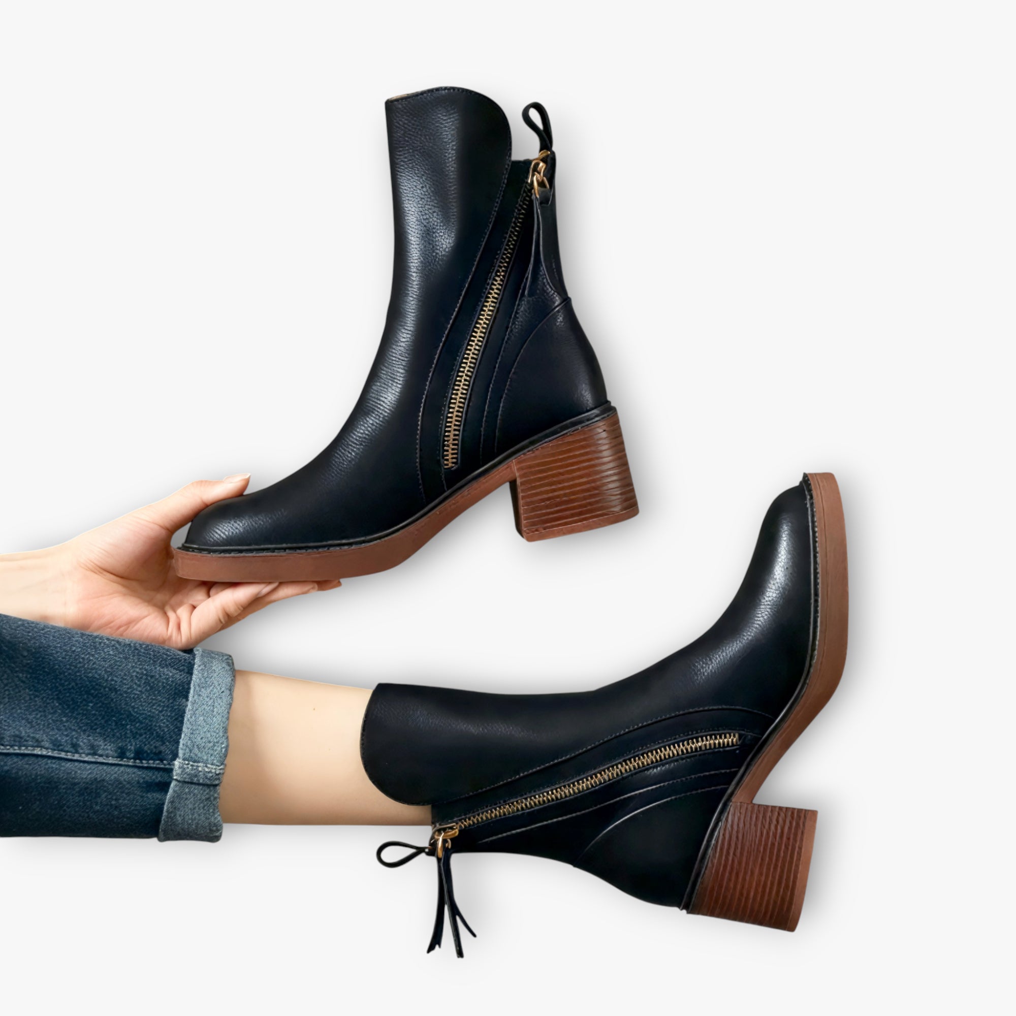 Black leather ankle boots with brown soles worn by a person on a white background