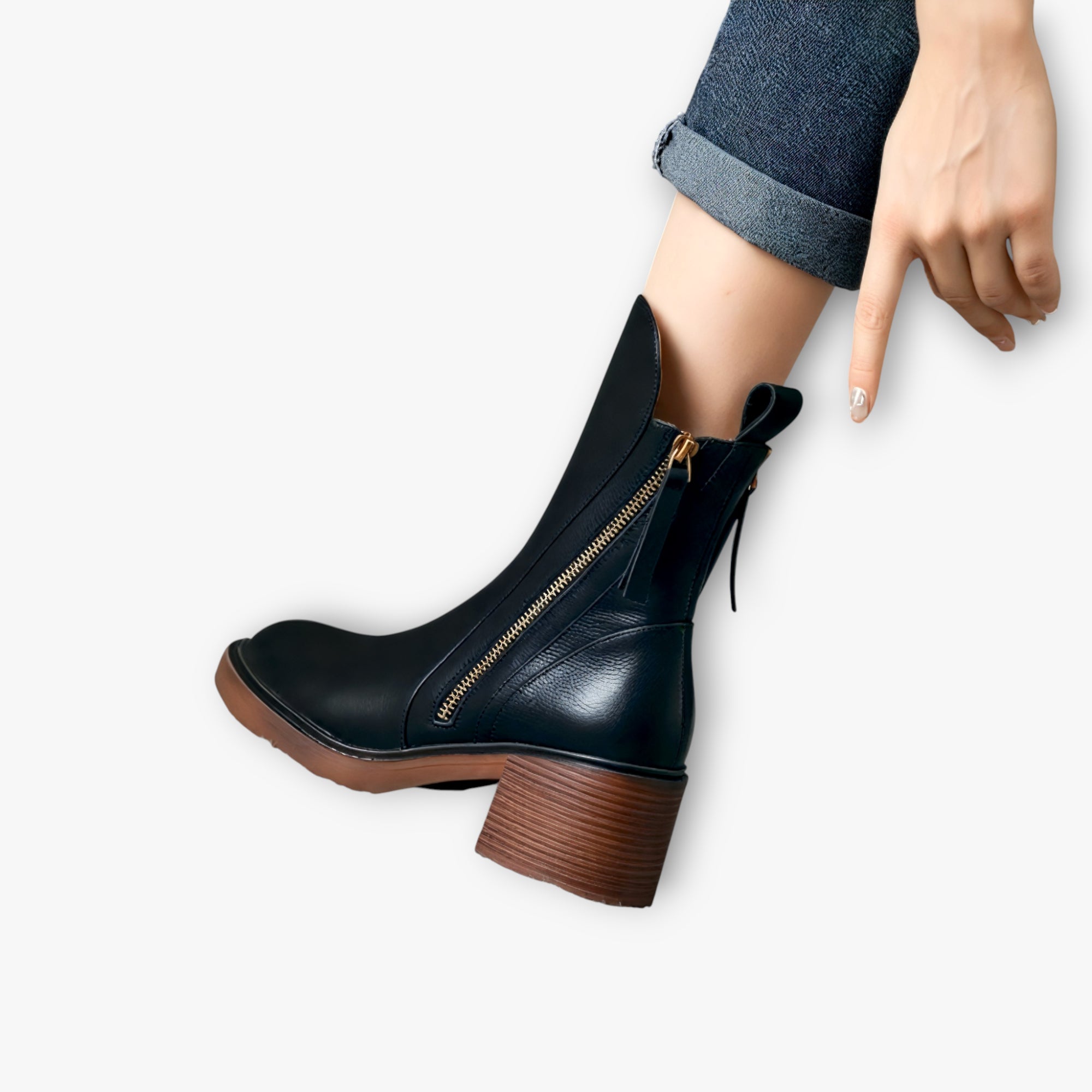 Black leather boot with brown sole worn by a person on a white background