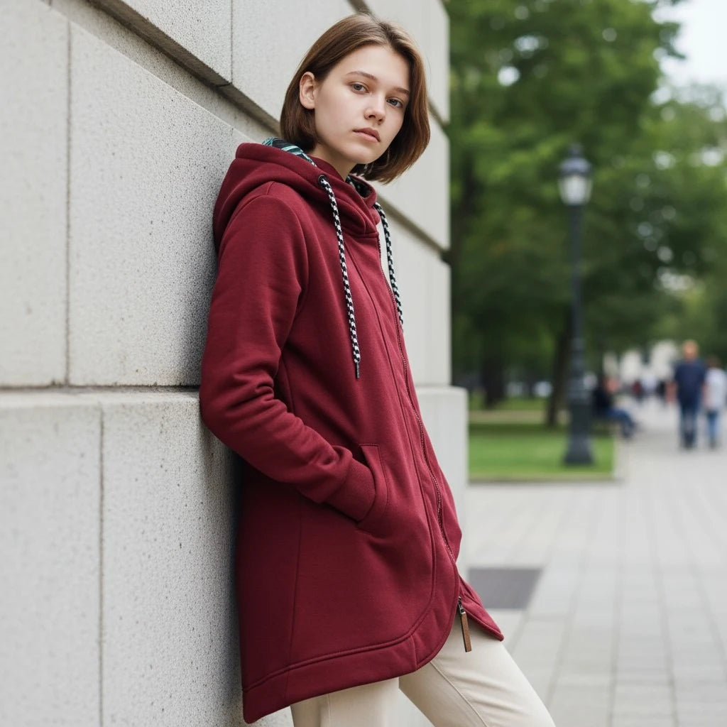 Person wearing a red hoodie leaning against a wall outdoors