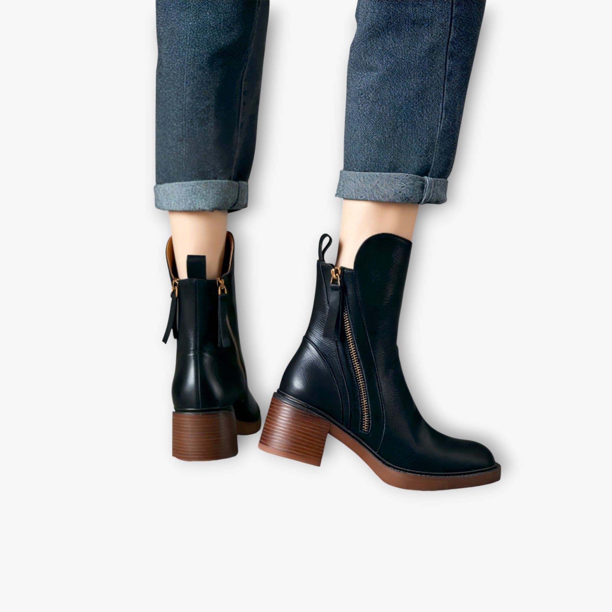 Black ankle boots with brown soles worn with rolled-up jeans on a white background